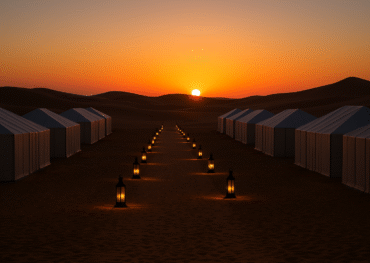Neatly aligned luxury tents in the Sahara Desert with lantern lights in a straight line, glowing at sunset in Merzouga, Morocco.