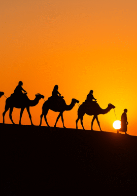 A caravan of camels with riders led by a Berber guide walking across the Merzouga dunes at sunset, captured in a realistic travel photo.morocco small group tours